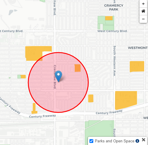 A map showing a red circle around a blue pin. The map also shows streets, building footprints in grey, and school properties in orange. The map is slightly zoomed out from the red circle to show nearby school properties in orange.