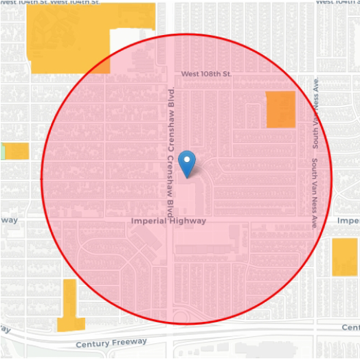 A map centered on a red circle around a blue pin. The map also shows streets, building footprints in grey, and school properties in orange