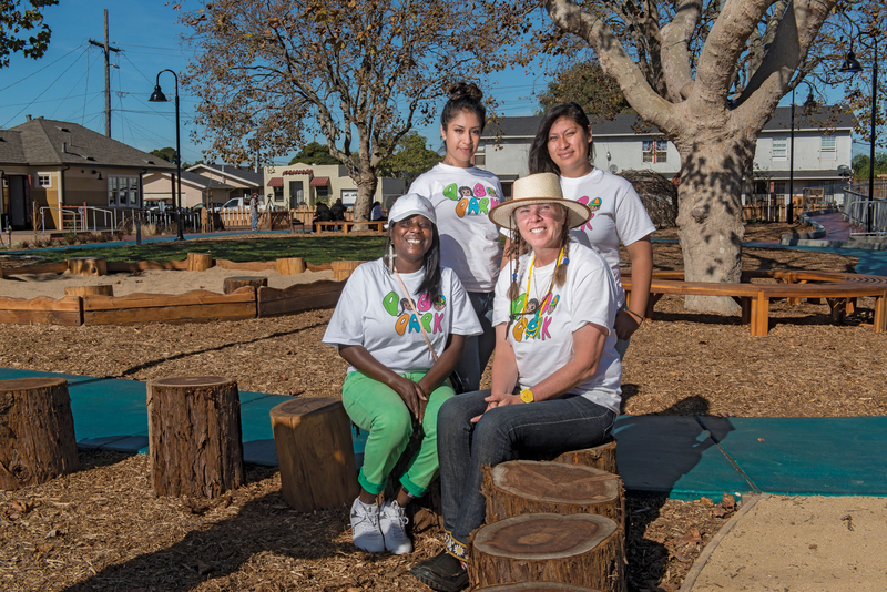 Four people sit on logs in newly established neighborhood park