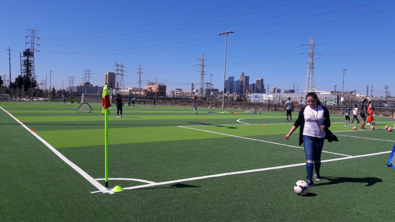 Woman retrieving soccer ball at edge of green soccer field in Albion Riverside Park