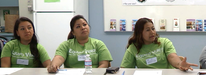 A group of people sitting on one side of a table wearing green t-shirts