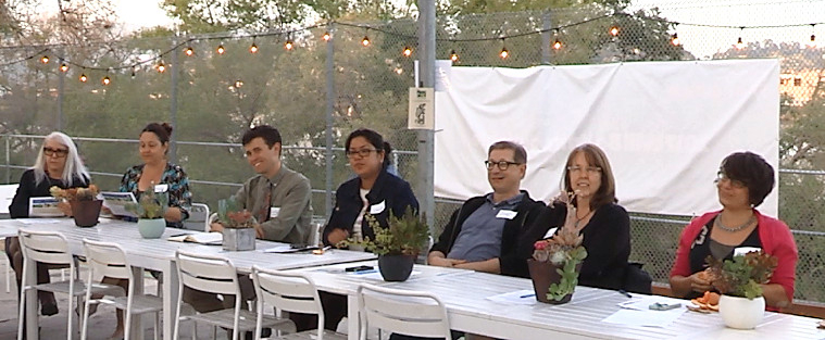 A group of people sitting on one side of a row of tables