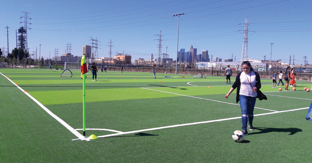 After construction, a woman follows a soccer ball on a green turf soccer field