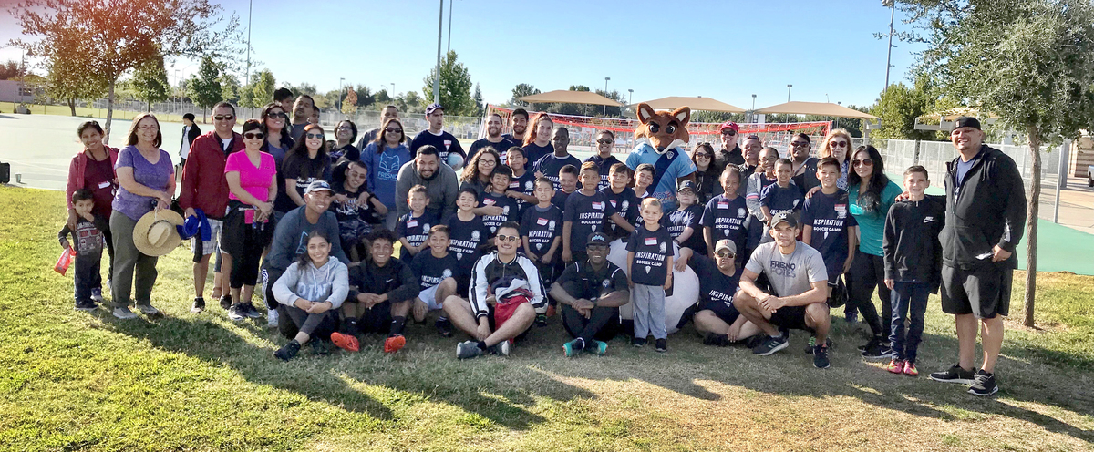 Kids wearing soccer camp gear, trainers and caretakers pose together outside for a photo