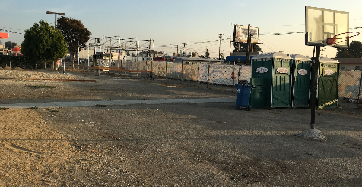 Dirt lot with two basketball hoops and three portable restrooms