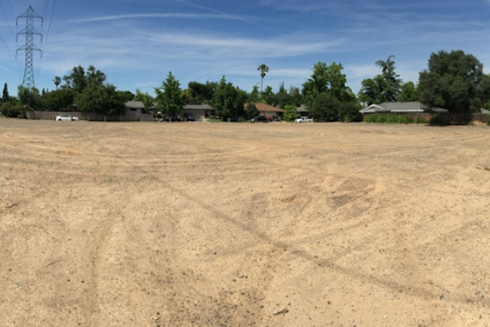 Dirt vacant lot with tire tracks and trees in the distance