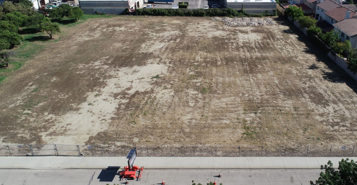 aerial view of fenced vacant dirt lot with tire tracks