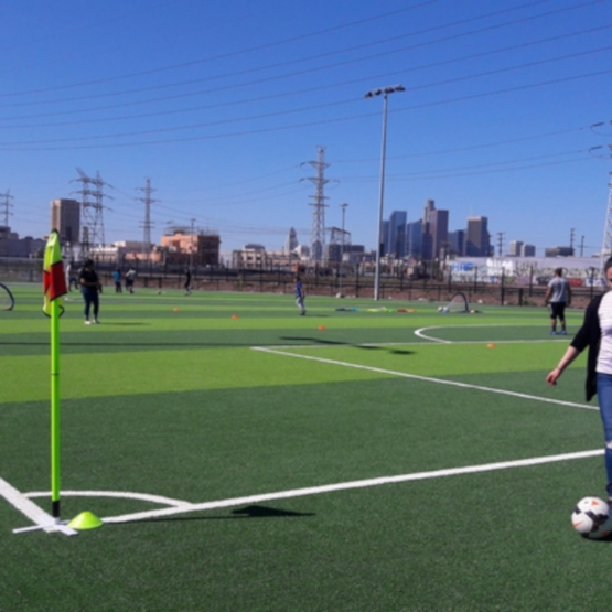 Woman retrieving soccer ball at edge of green soccer field in Albion Riverside Park