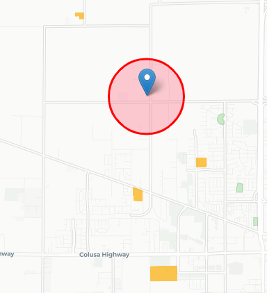 A map showing a red circle around a blue pin. The map also shows streets, building footprints in grey, parks in green, and school properties in orange. The map is slightly zoomed out from the red circle to show nearby school properties.