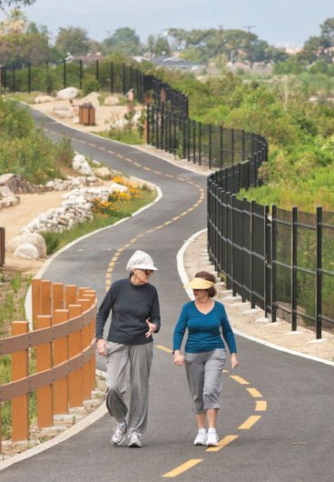 Two women walk and talk along a paved bike path edged with a black metal fence