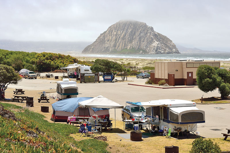 Tents and campers in Morro Dunes RV Park with Morro Rock in the Pacific Ocean in the background