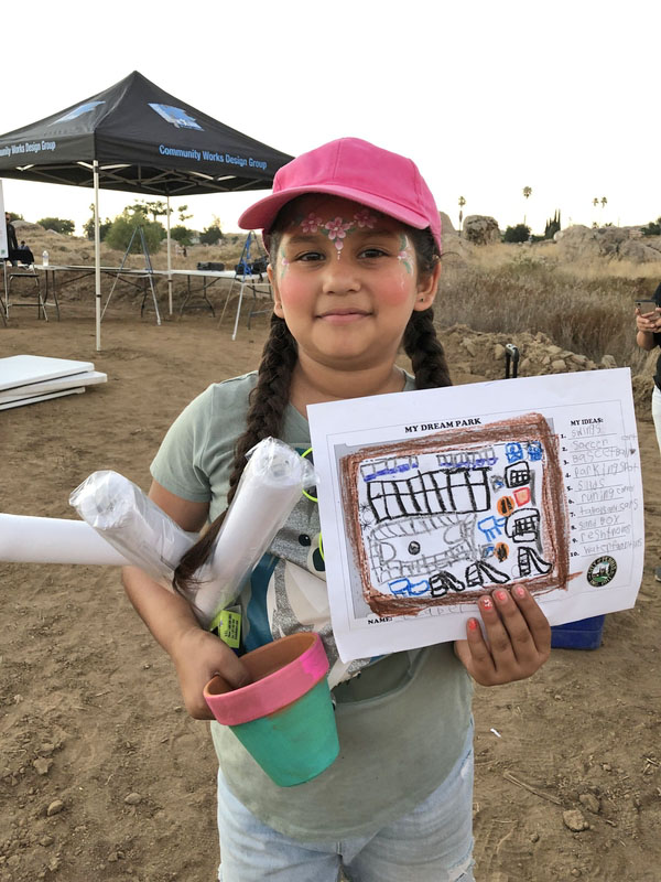 Young girl with face paint holding a paper with a drawing showing her dream park