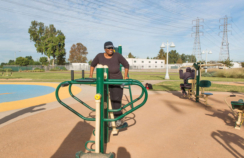 A woman smiles and uses new exercise equipment in an outdoor exercise area