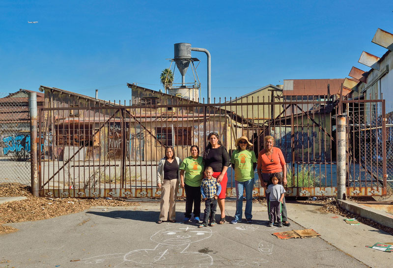 A group of woman and children standing on blacktop in an industrial area and future park location