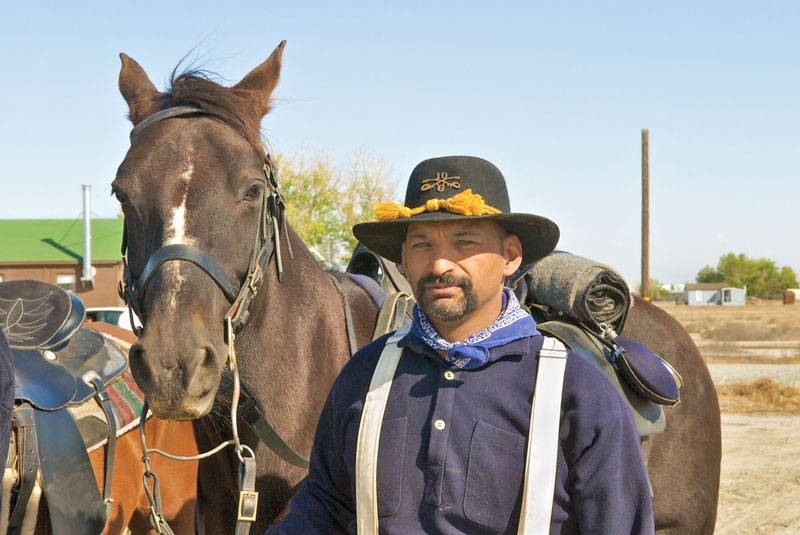 A man wearing early 1900's settler's reenactment clothing standing beside a horse