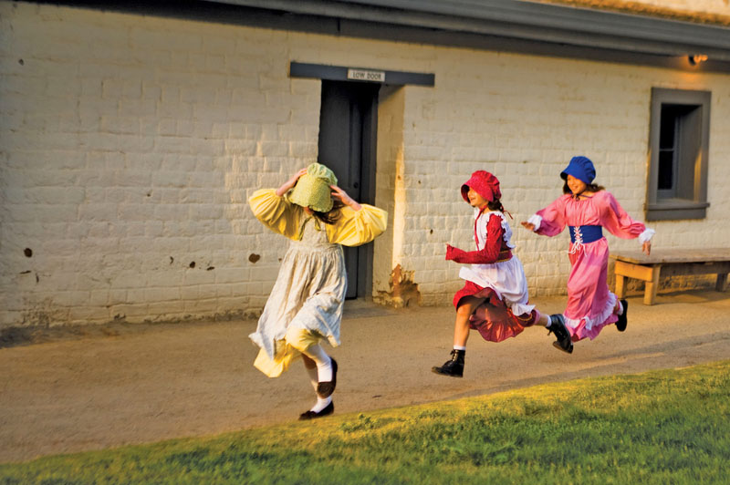 Three girls running and wearing historical reenactment clothing and bonnets