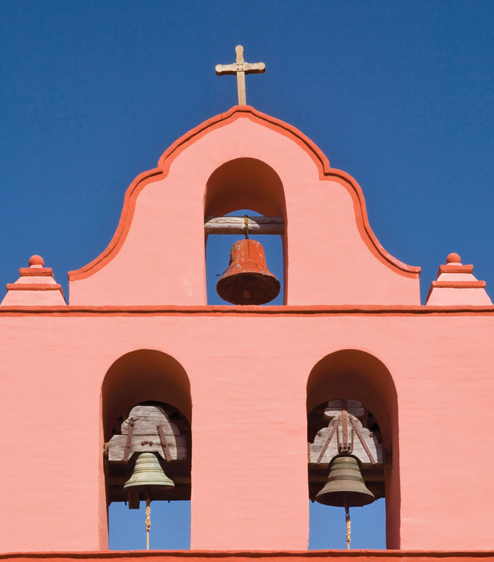Three mission bells and a cross at the top of the pink La Purisima Mission