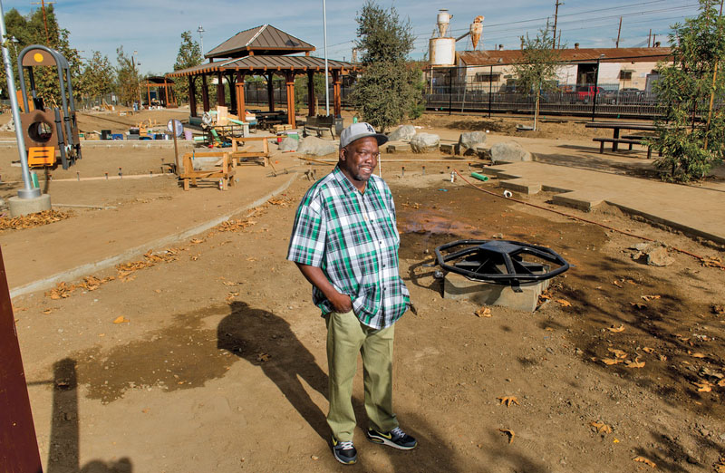 A smiling man stands on an area of compact dirt in the middle of a new park construction
