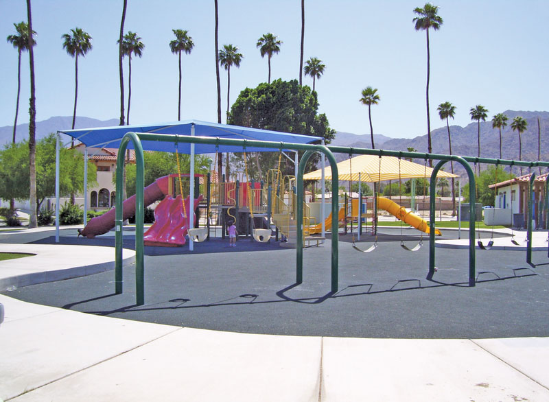 A new swingset and slides at a park surrounded by palm trees