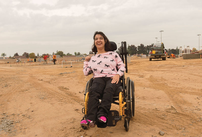 A smiling woman in a wheelchair on compact dirt where a new park is being built