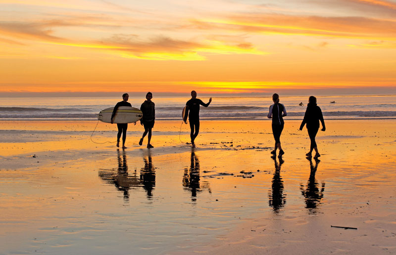 Surfers gather on the beach as small waves crash on the sand at sunset