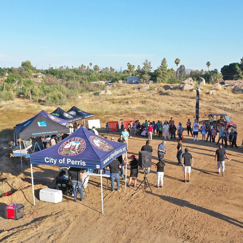 Over 50 individuals of all gender and ages gathered in a circle in a vacant dirt lot