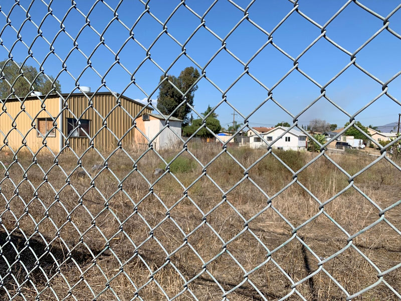 Vacant lot with overgrown grass behind a chainlink fence.