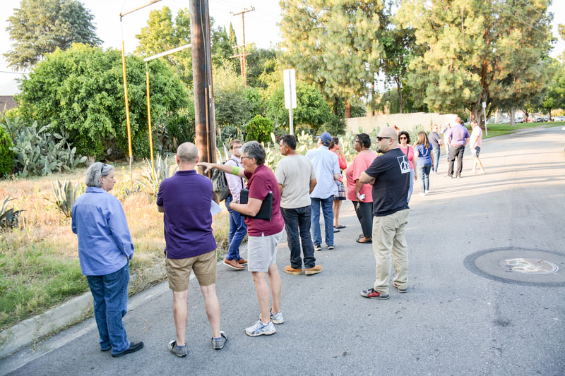 Group of people standing on a road overlooking a grassy lot and talking