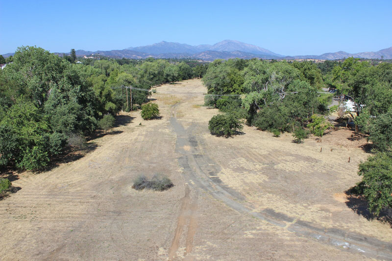 Aerial image of large vacant dirt lot surrounded by tall trees.