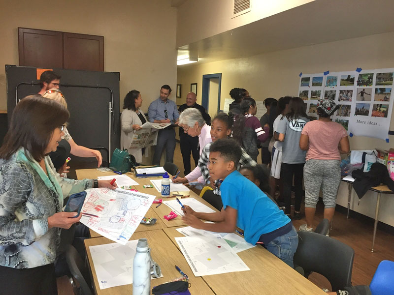 Adults and kids review images pin up on a wall and work on prints of the park on a nearby table.