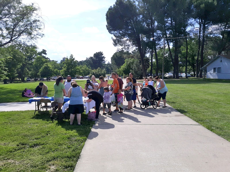 Group of people of different ages gathered on a sidewalk with folding tables