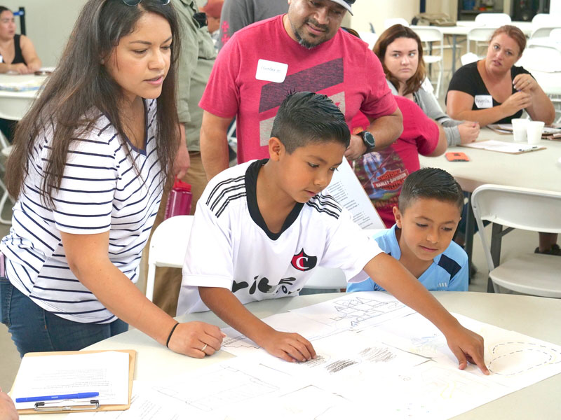 Two kids and a woman look over a large print of a park.