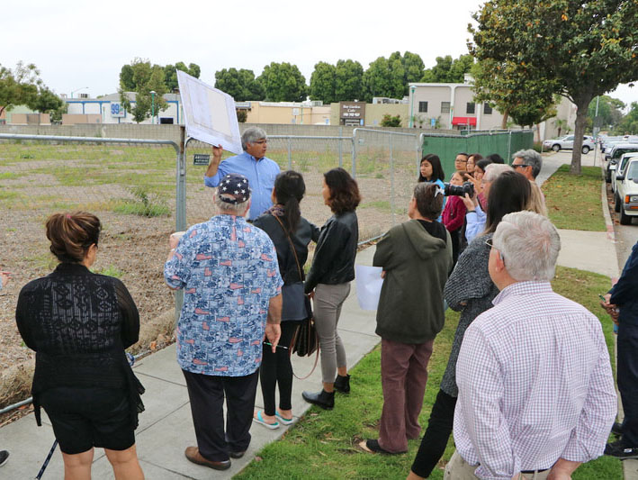 Group of people standing on a sidewalk listening to a presenter holding an image of the park site