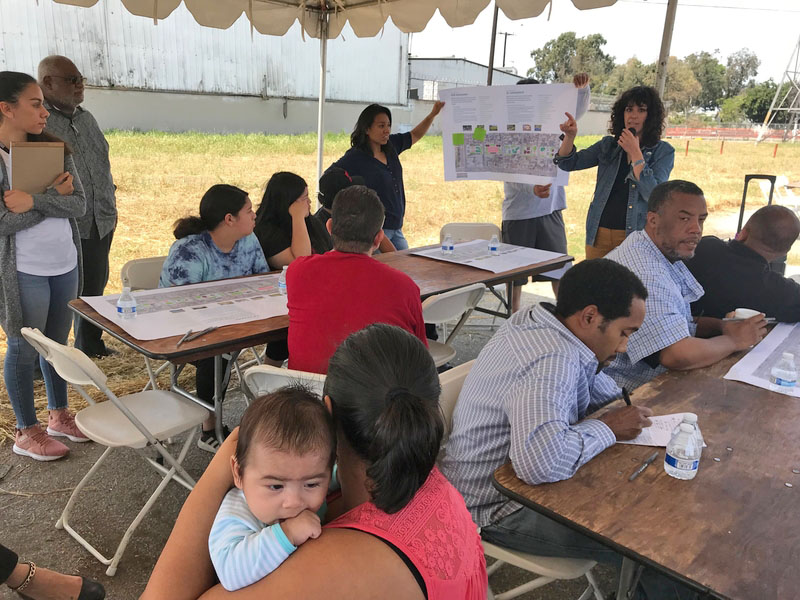 Groups of people drawing at tables while listening to a presenter holding an image of the park site