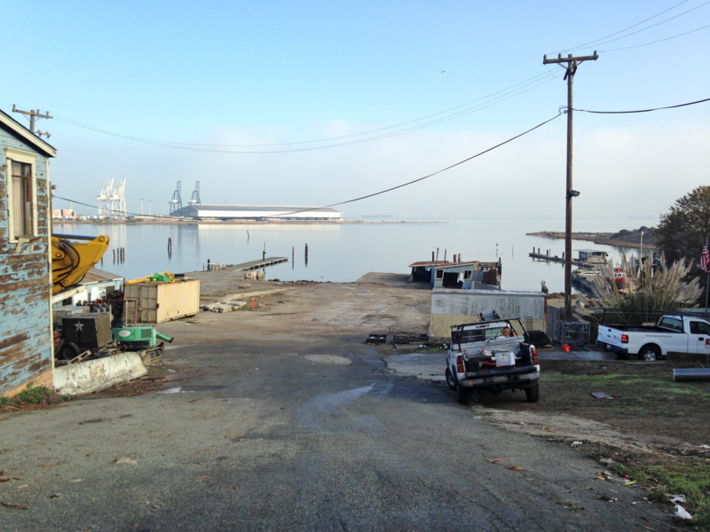 Vacant lot with pick up trucks and power lines near water by a bay.