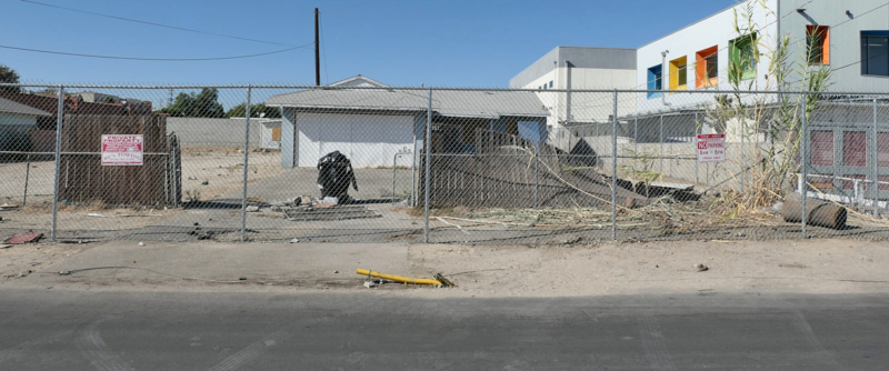 Vacant lot with an old house fenced-off with a chainlink fence.