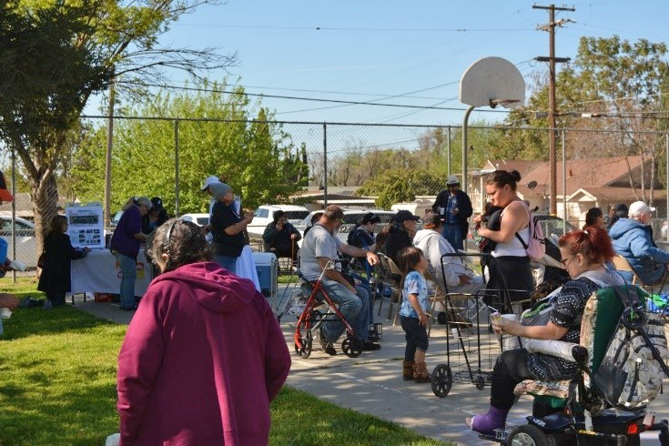 Groups of people standing and sitting outside under a basketball hoop.