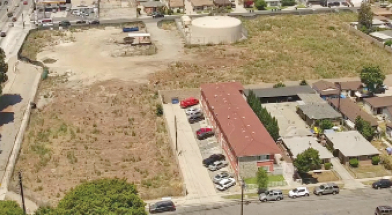 Aerial image of vacant lot near a long building with angled parking spots.