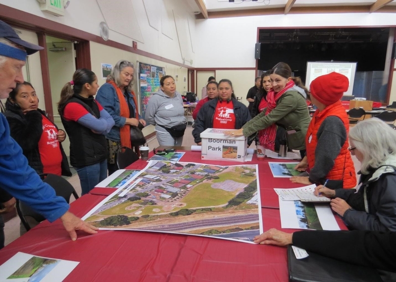 People gathered inside around a long table with an big print of the park site.
