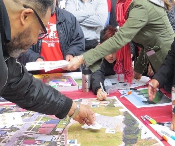 Man putting a post it on a big print of a park while a young boy draws on the print.