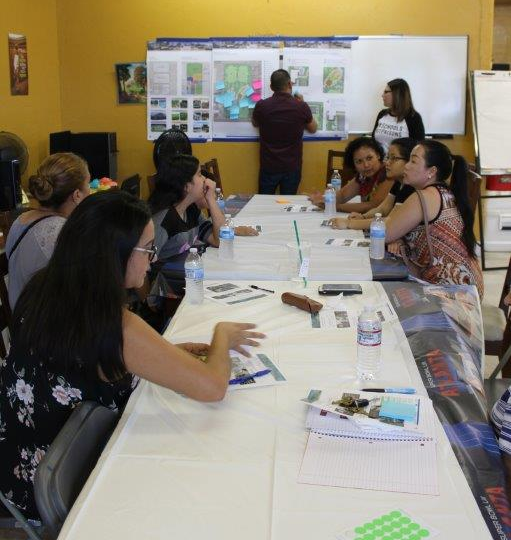 Group of women gather at a table as two people in the front discuss printed boards with sticky notes