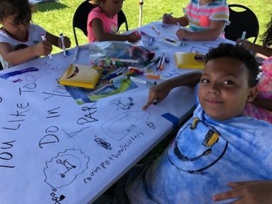 young boy smiling and pointing at drawing on table that has been covered with drawing paper.