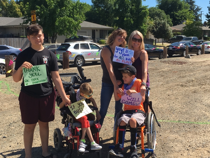 Two women, one young adult and two boys using wheelchairs hold signs in support of building a park.