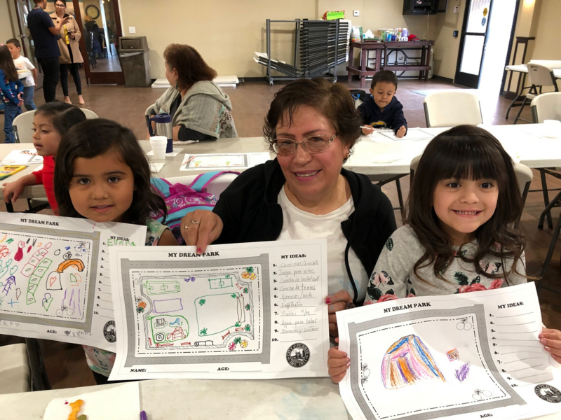 Woman and two young girls holding drawings of their dream parks.