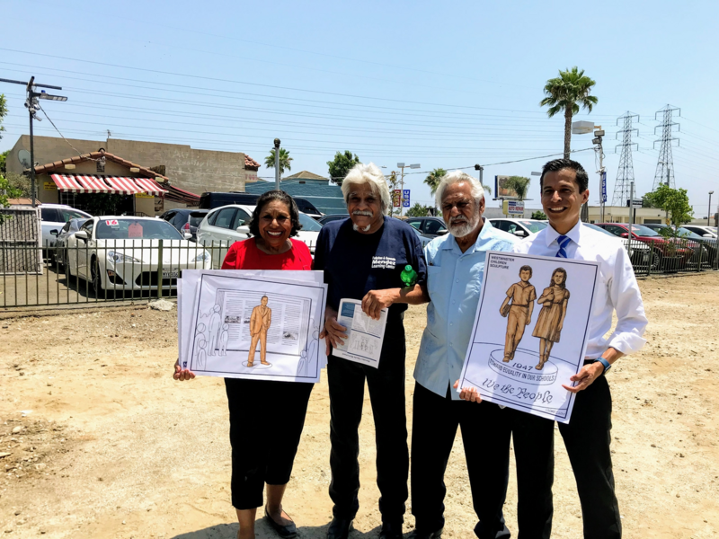 Four people standing on a vacant lot holding images of proposed sculptures and art for the park.