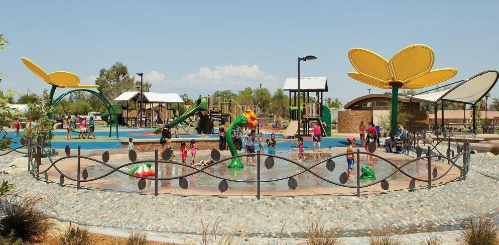 After construction, kids in a water play area with an iron gate shaped like a vine with leaves