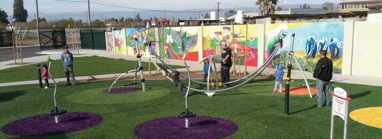 Kids and adults playing on a metal structure in front of a mural of mariachi singers and birds