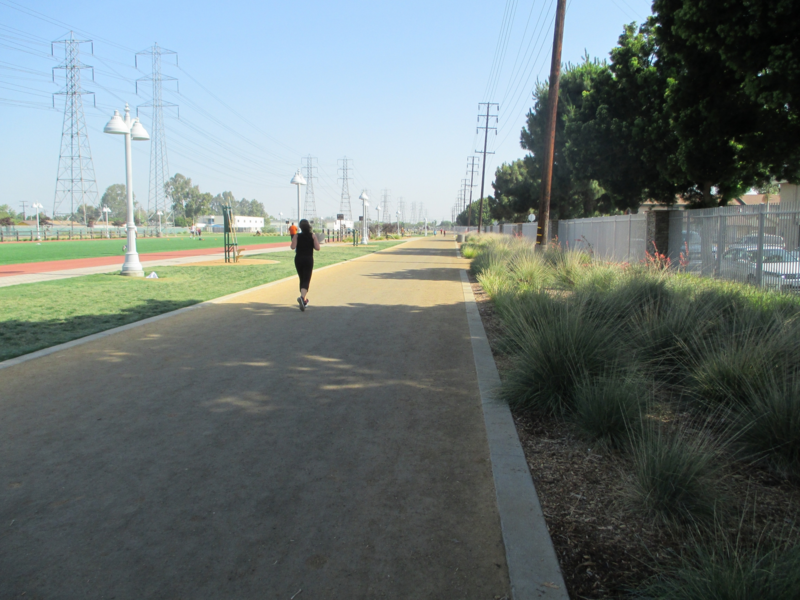 Woman running on dirt track next to landscaped plants and grassy areas.