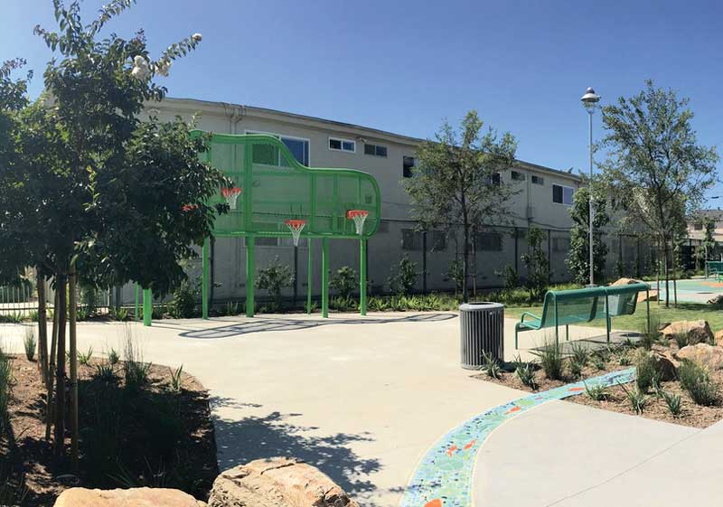 Outside basketball court with multiple hoops, nearby bench, and trees.