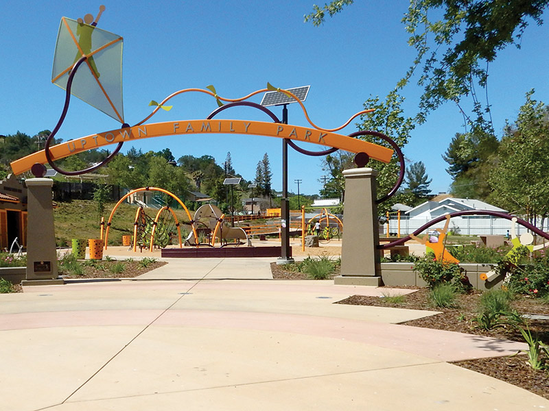 Cement and metal park entrance with squiggly lines and letters that read Uptown Family Park.